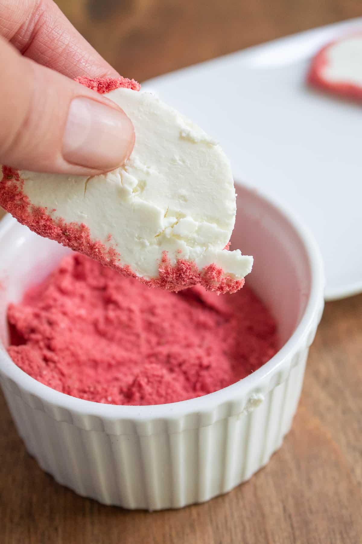 Dipping a round of goat cheese into the crushed strawberry powder.