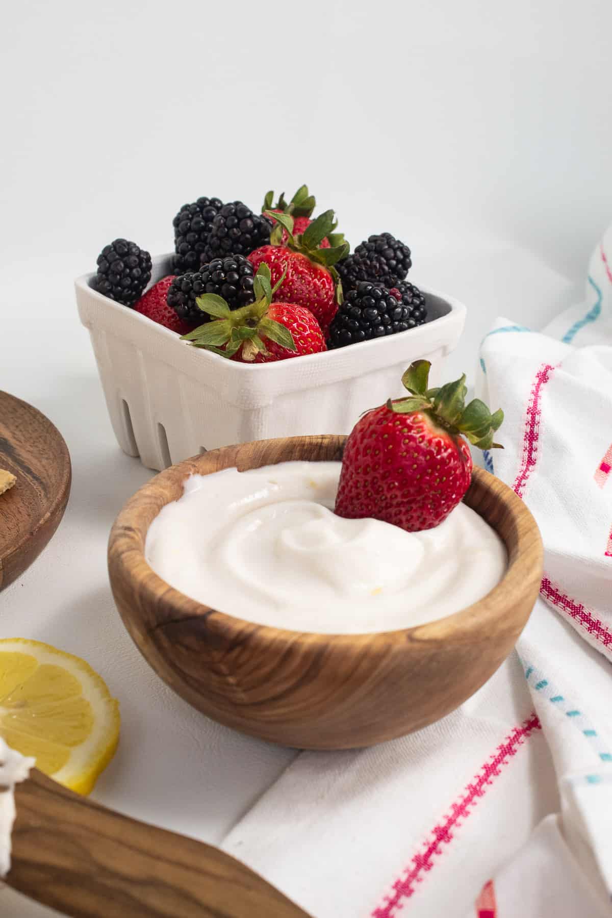 The fruit dip in a wooden bowl with a strawberry is at the center of the image with berries in a basket nearby.