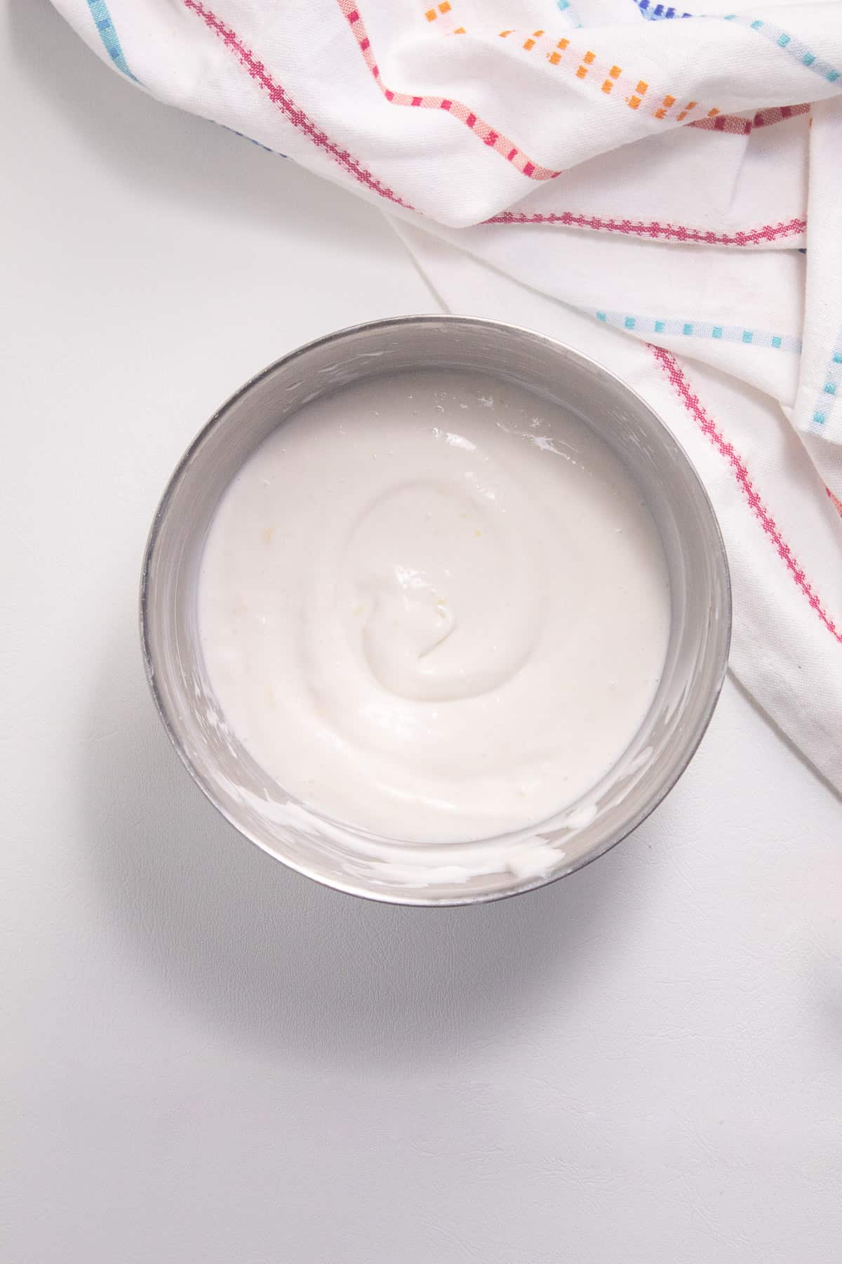 The finished dip is swirled in the bottom of a silver bowl on a white surface.