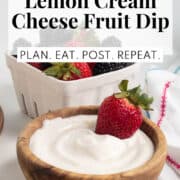 The fruit dip in a wooden bowl with a strawberry. The words, " lemon cream cheese fruit dip" and "plan. eat. post. repeat." are in a white box at the the top of the image.