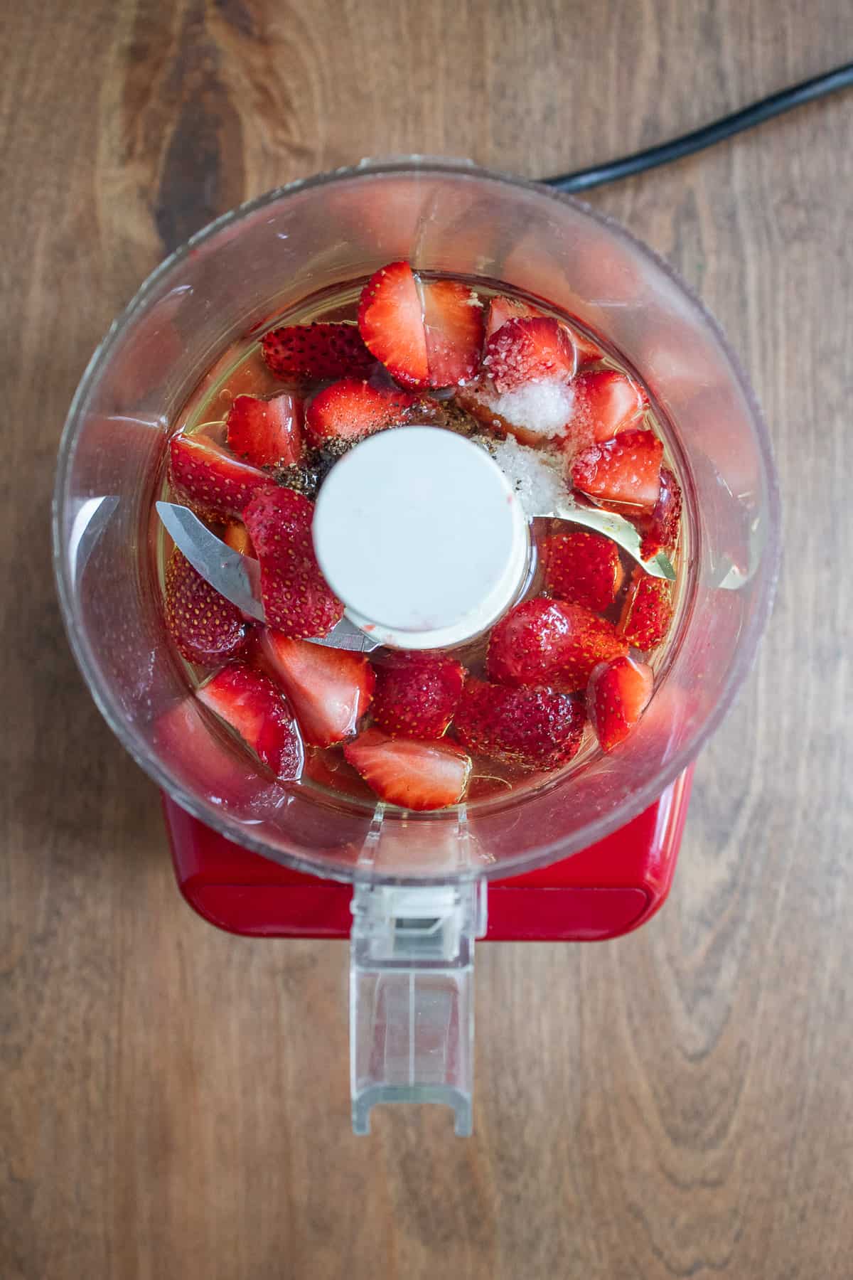 Strawberries, oil, vinegar, salt, and pepper in the bowl of a mini food processor.