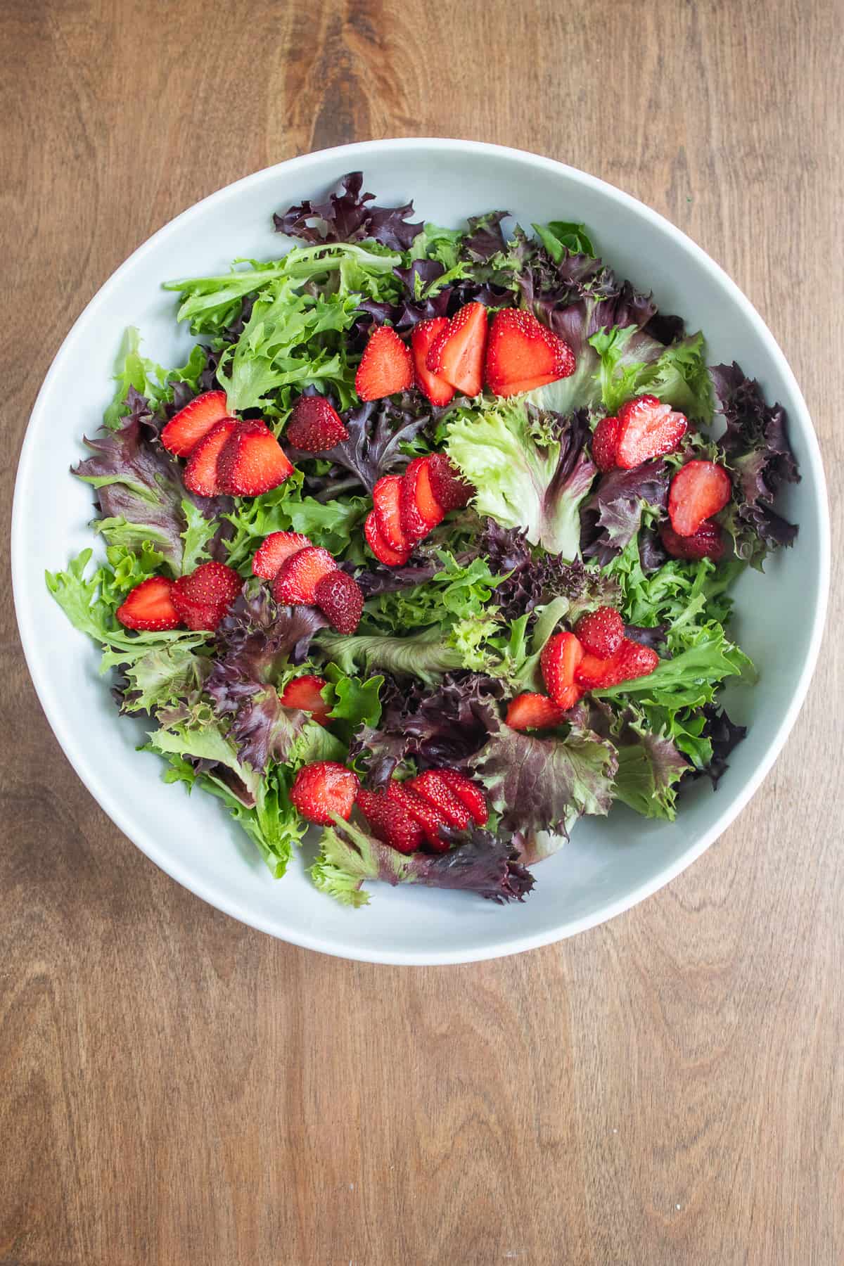 Fresh strawberries are scattered over a bed of mixed greens.