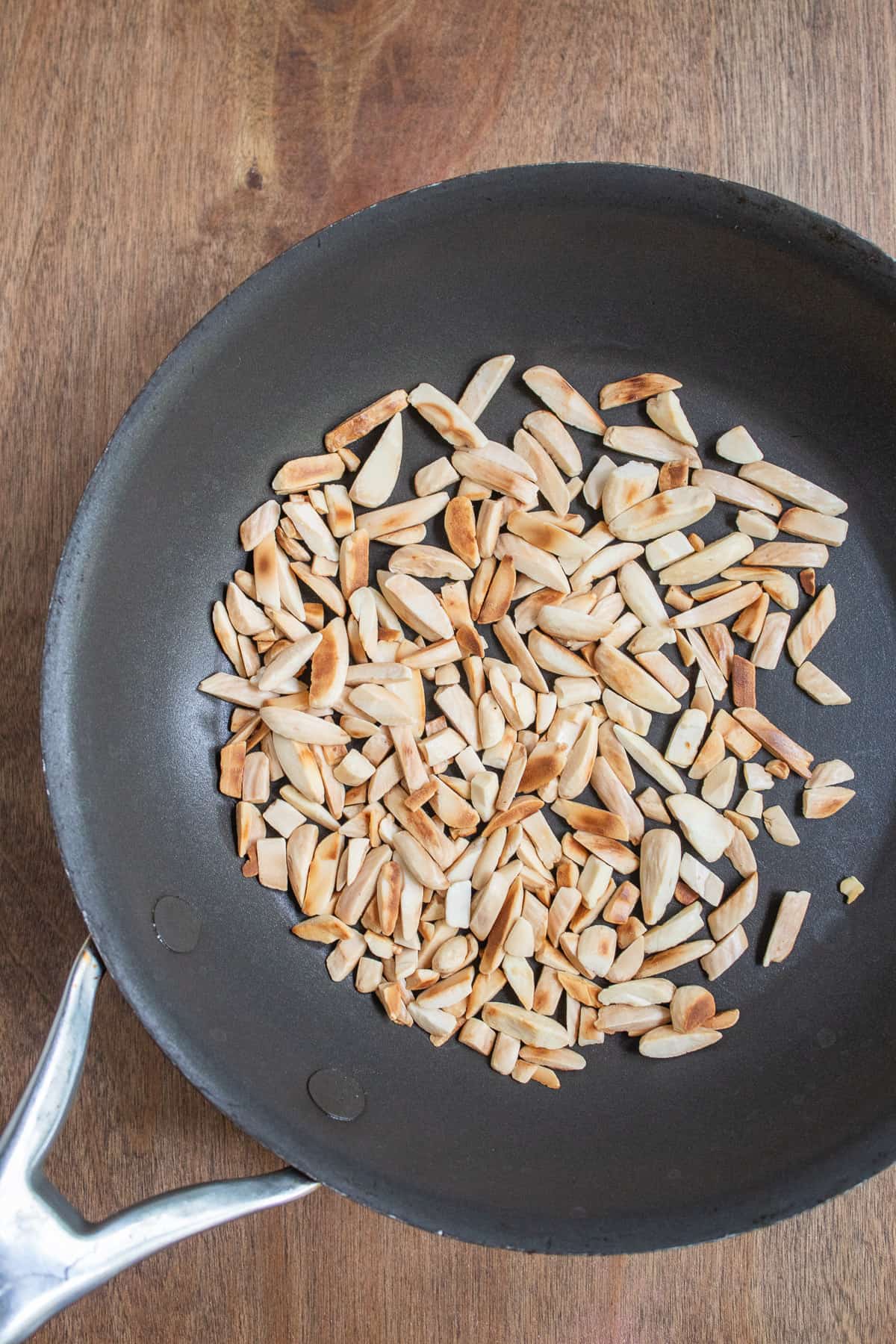 Toasted slivered almonds sit in a black skillet.