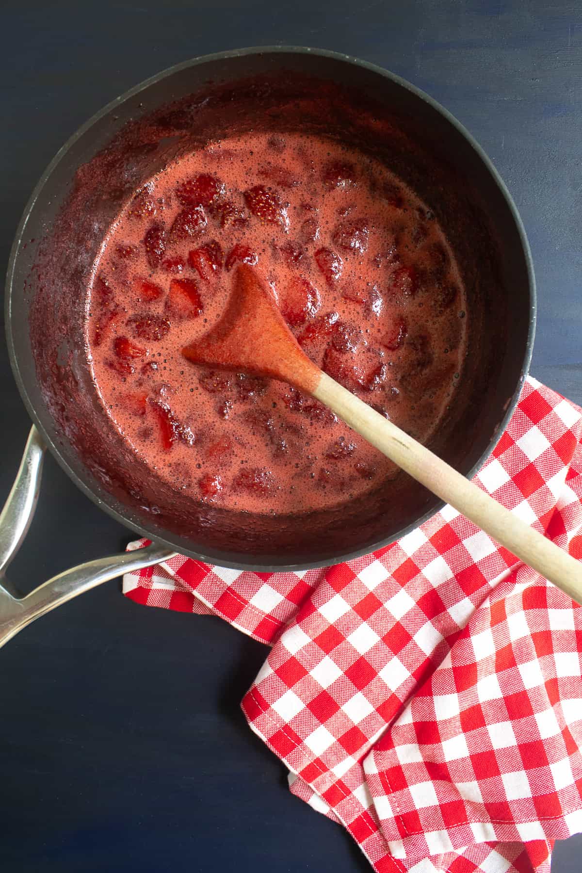 The cooked strawberries are in the bottom of a black saucepan.