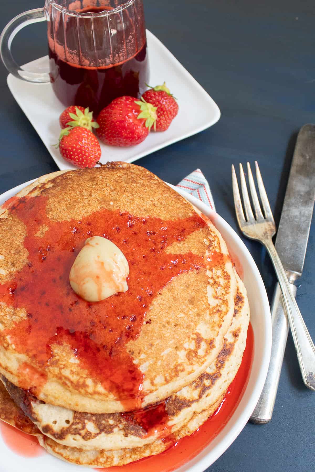 A stack of pancakes is drizzled in strawberry syrup on a white plate.