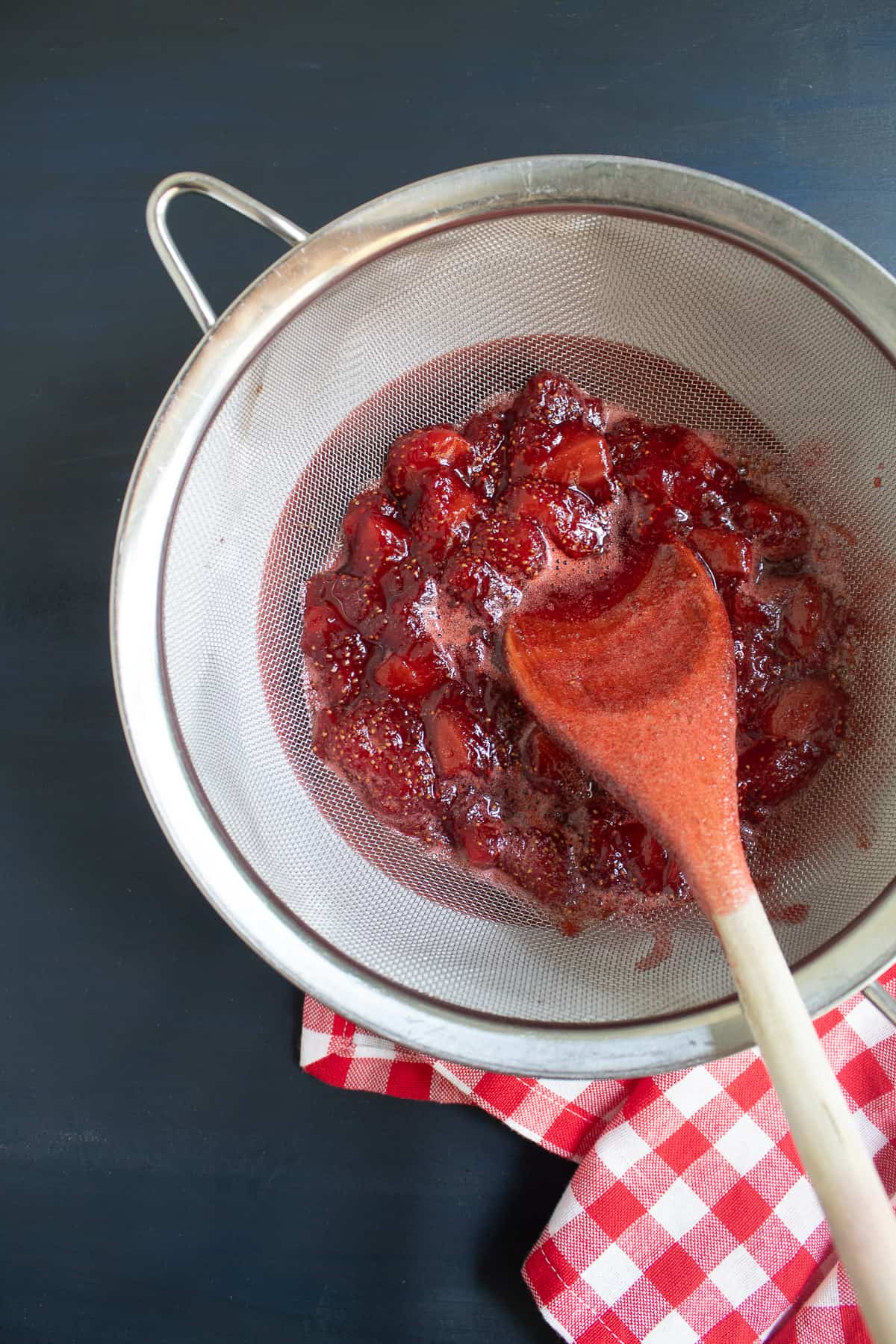 Strawberries are strained out of the syrup with a mesh colander.