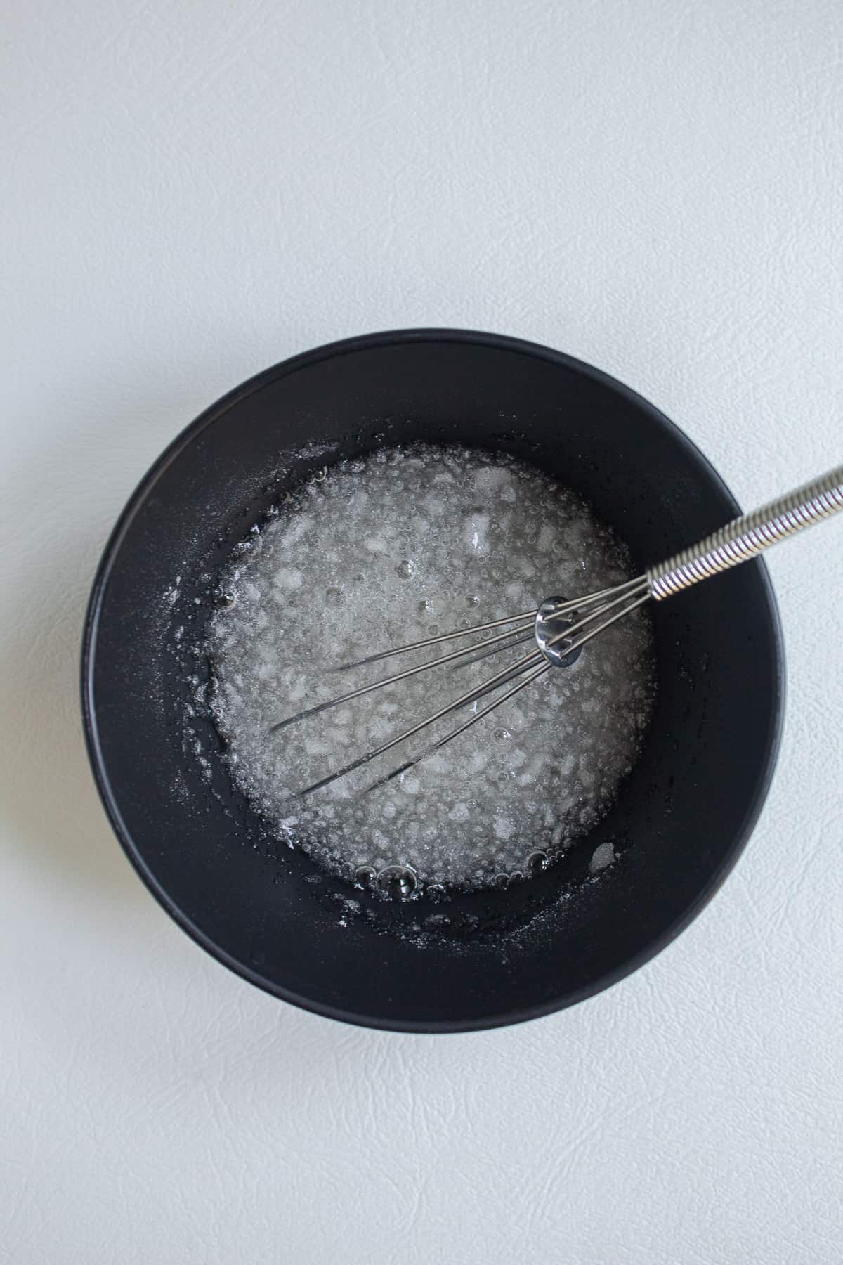 Powdered gelatin and water are combined in a small black bowl and whisked together.