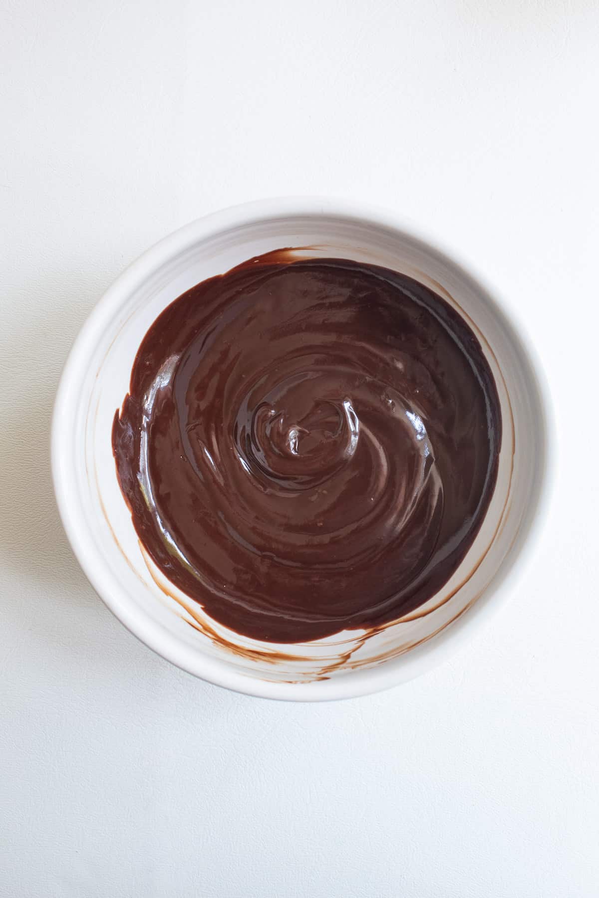 The finished ganache is swirled in the bottom of a small white bowl.