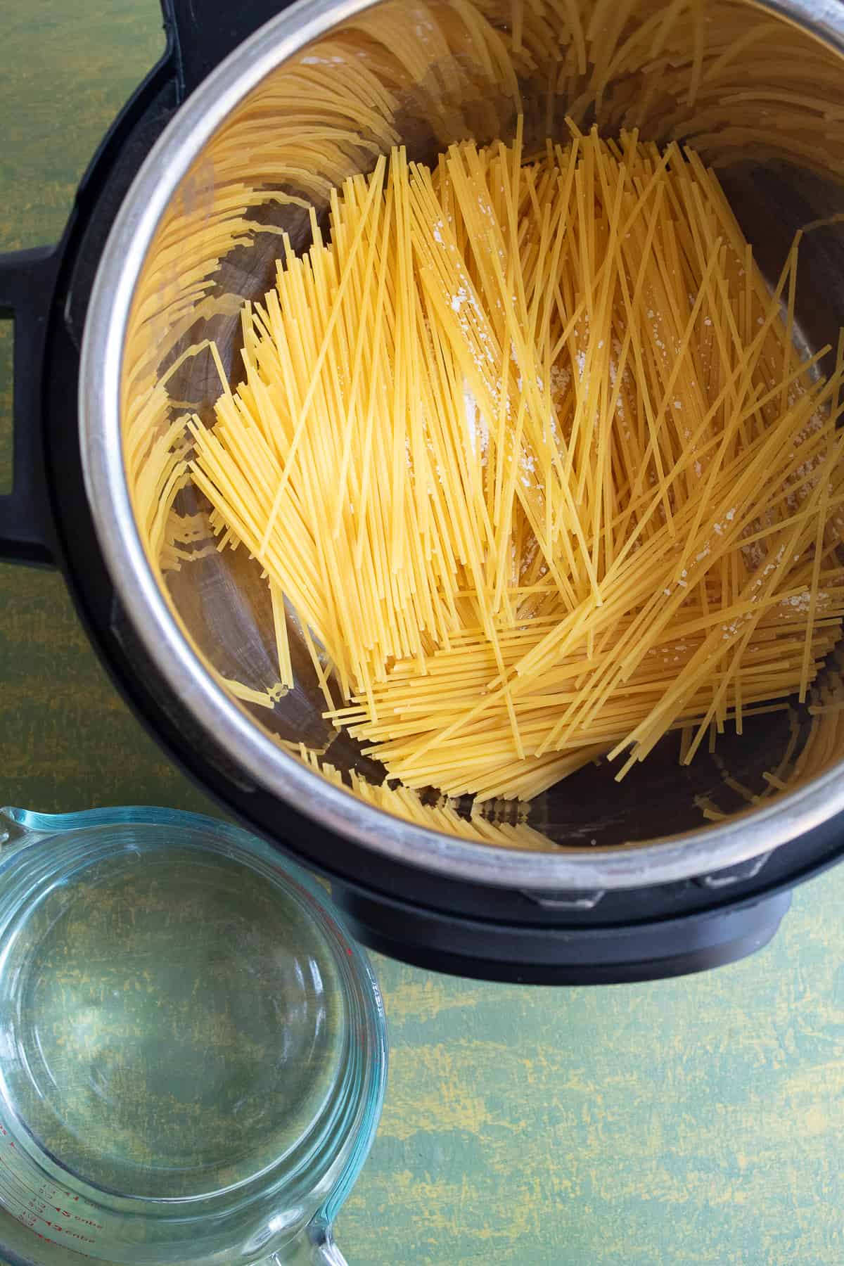 Uncooked spaghetti is broken in half and placed in the bottom of the Instant Pot.