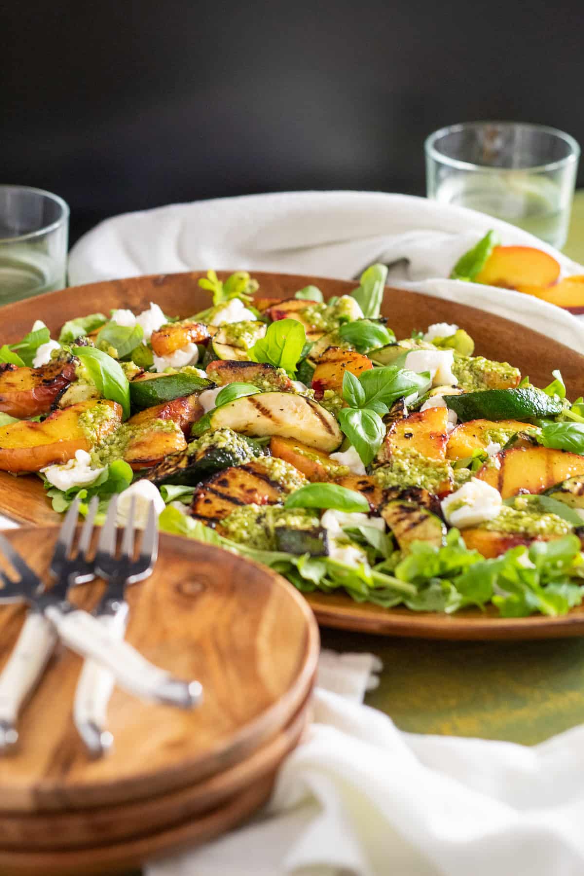 A wooden platter displaying the salad sits on a green table with a black backdrop.