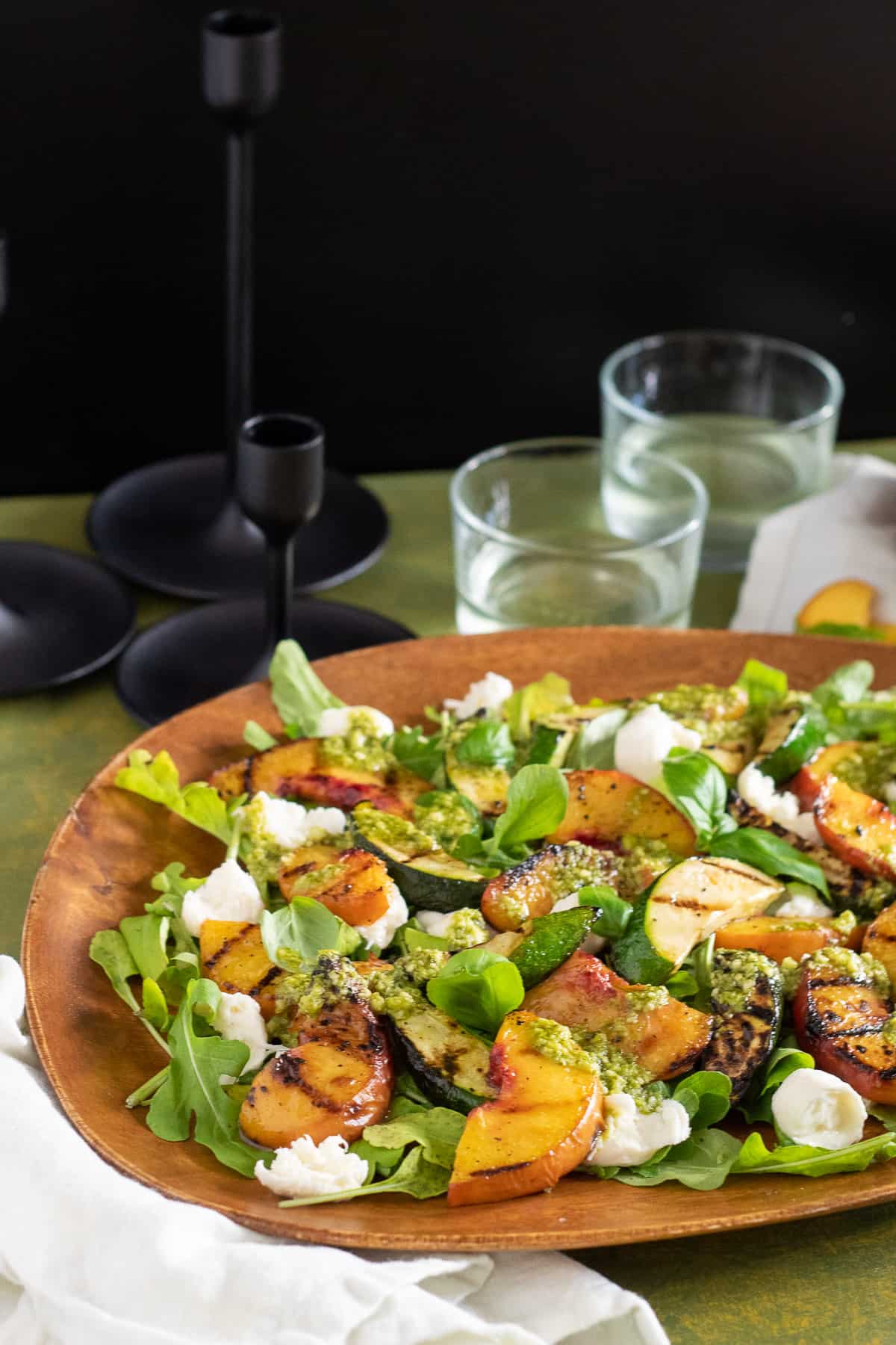 A wooden platter displaying the salad sits on a green table with a black backdrop.