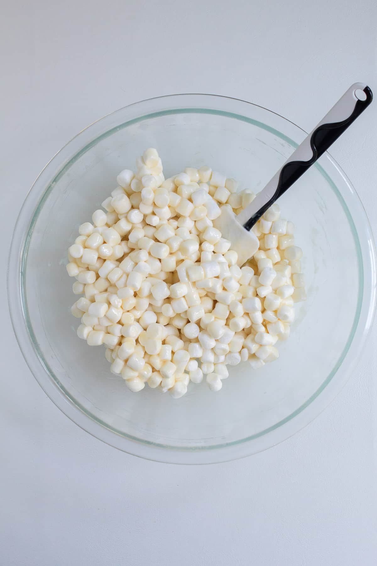 The marshmallows are coated with the melted butter mixture in the bottom of a large glass bowl.