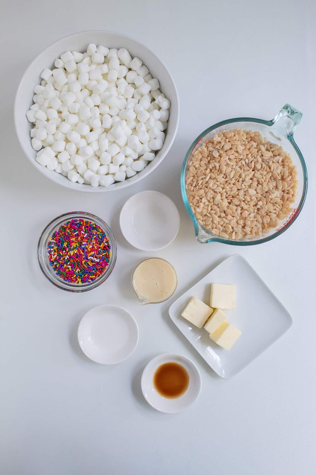 The ingredients for the treats are arranged on a white surface in various bowls and plates.