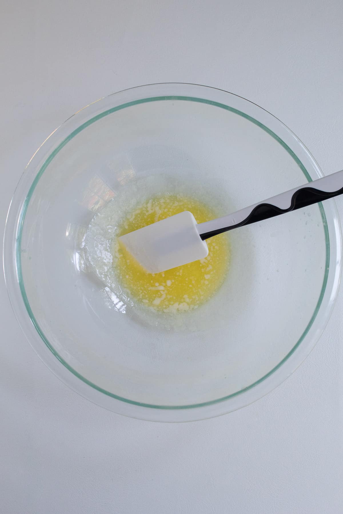 Melted butter and a flexible spatula sit in the bottom of a large glass bowl.