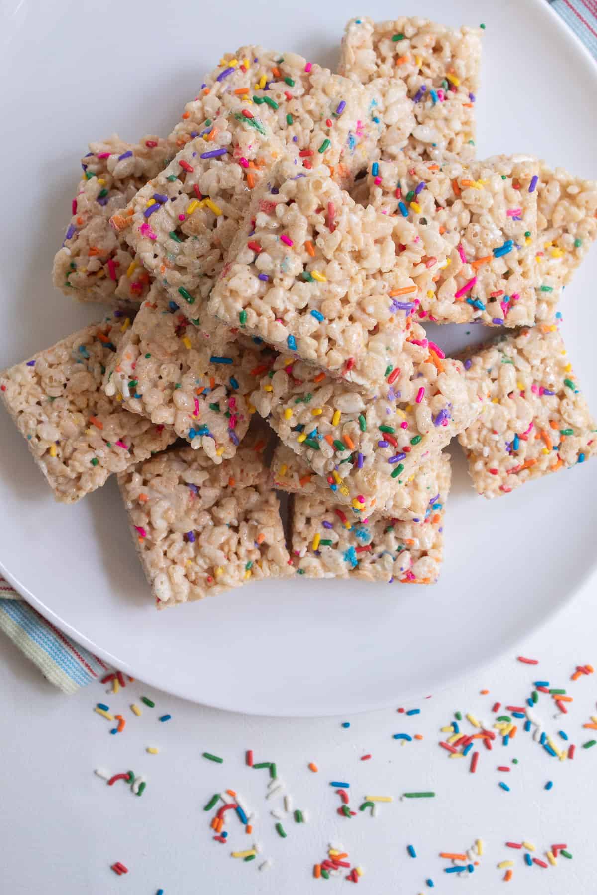 The treats are stacked high on a white plate over a surface scattered with sprinkles.