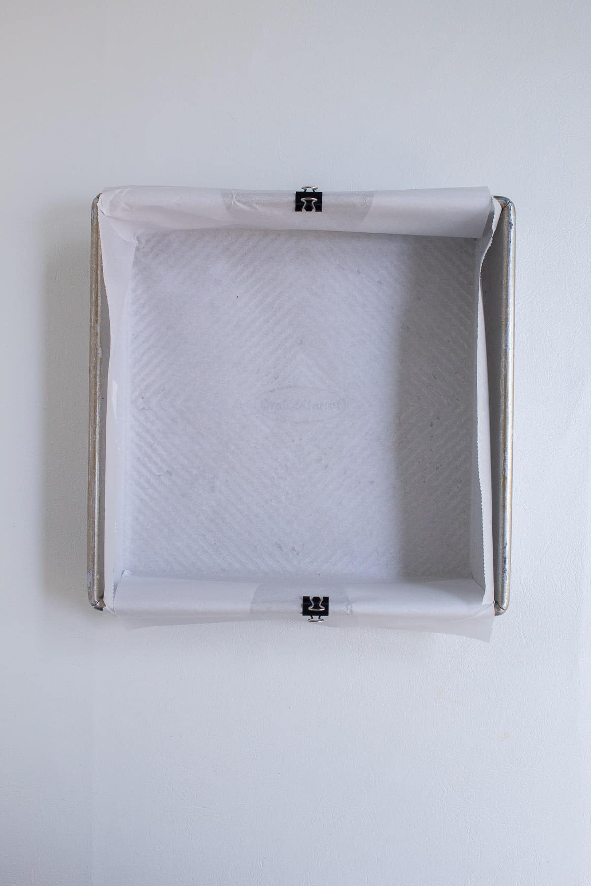 A square pan is lined with parchment and two edges are clipped to the pan sides with binder clips.