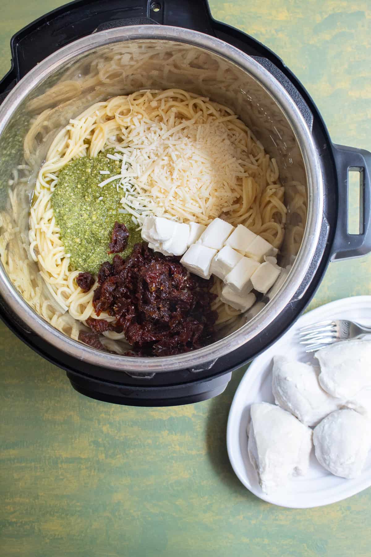 The cooked spaghetti is combined with sundried tomatoes, pesto, cream cheese, and Parmesan cheese in the insert of the Instant Pot.