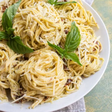 A detail image of the spaghetti twirled into piles on a white platter and garnished with basil leaves.