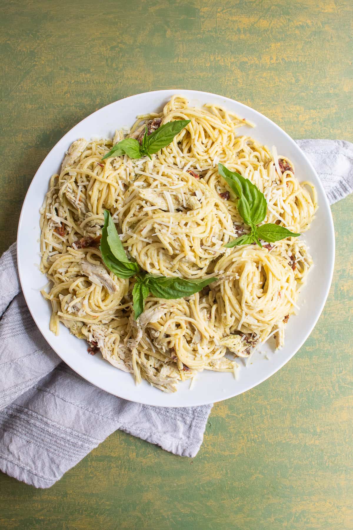 An overhead shot of the spaghetti twirled into piles on a white platter and garnished with basil leaves.