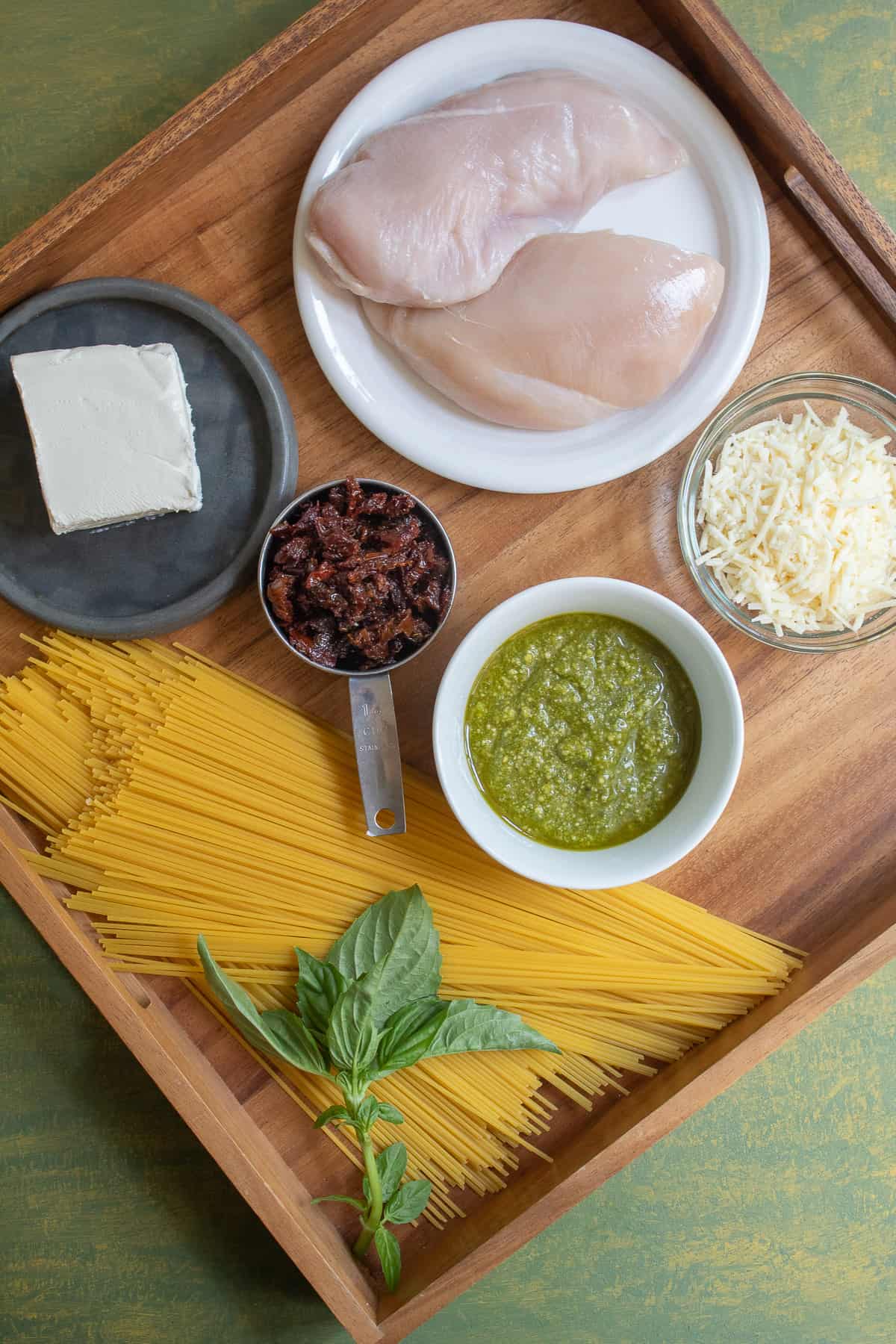 The ingredients for the chicken spaghetti are displayed on a wood tray on top of a green surface.