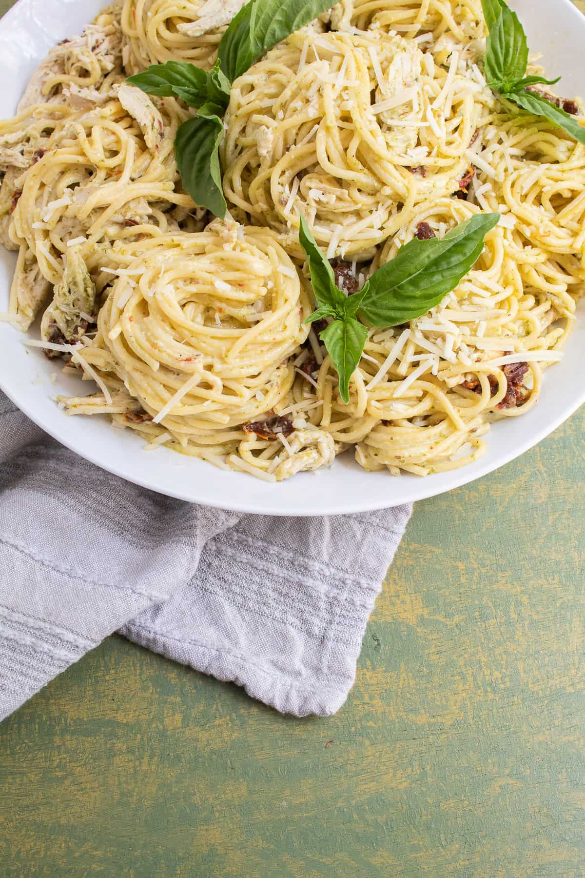 The spaghetti twirled into piles on a white platter and sitting on a green surface is garnished with basil leaves.