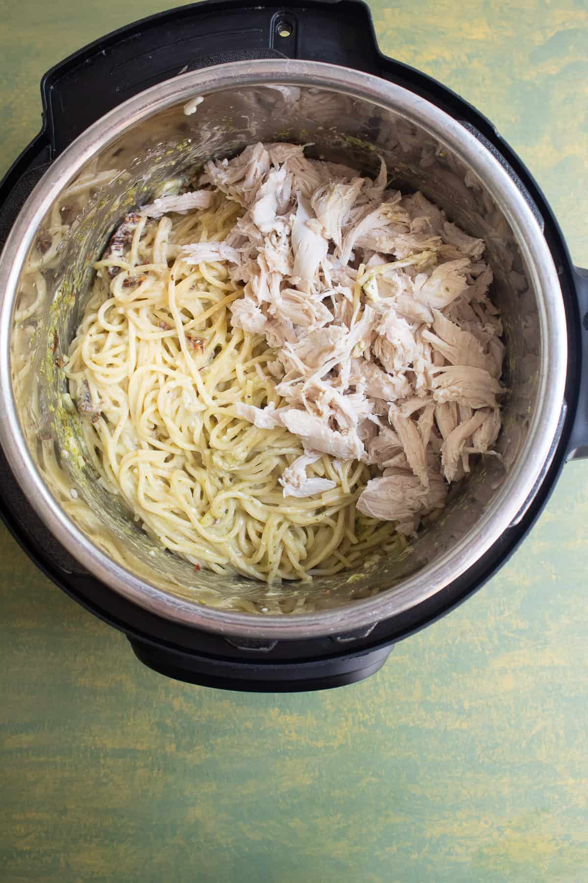 The cooked spaghetti and shredded chicken in the insert of the Instant Pot.