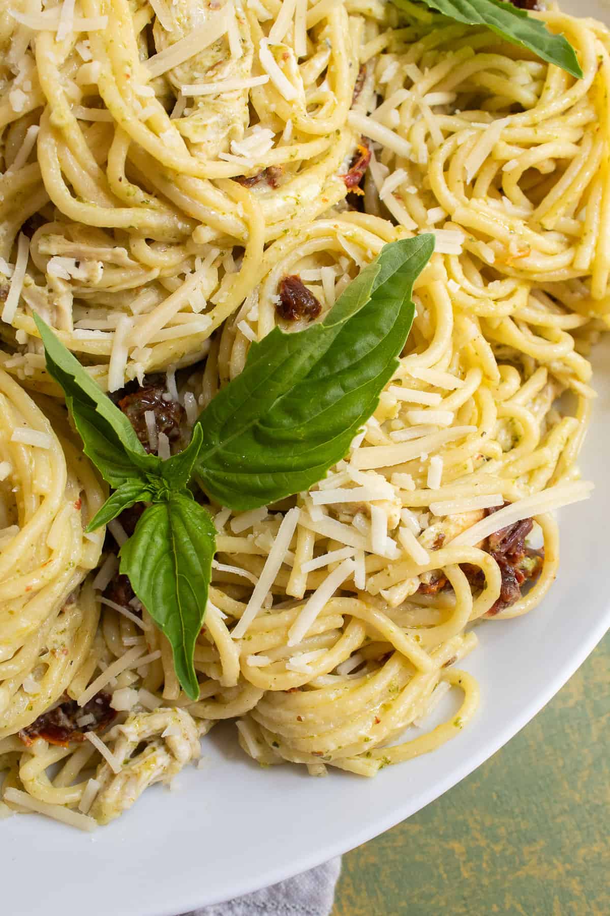 A close-up of the texture of the twirled spaghetti with shredded cheese and basil leaves as garnish.