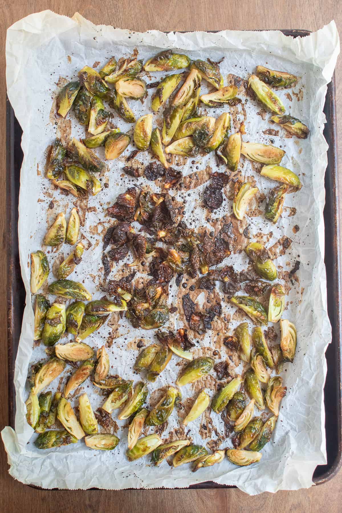 The brussel sprouts sit on a parchment-lined sheet pan after roasting. Some are deeply caramelized.