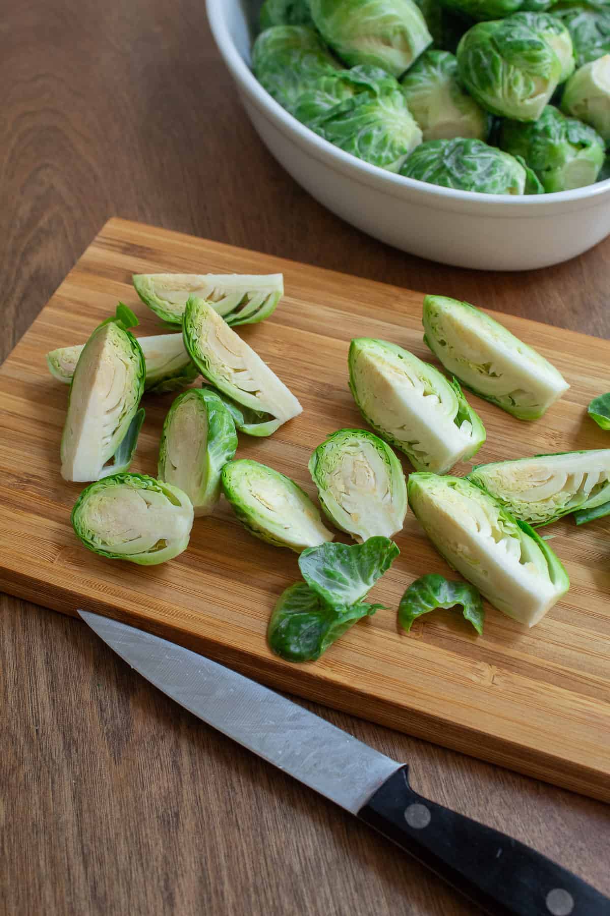 Brussel sprouts are cut into halves or quarters, depending on size, on a bamboo cutting board.