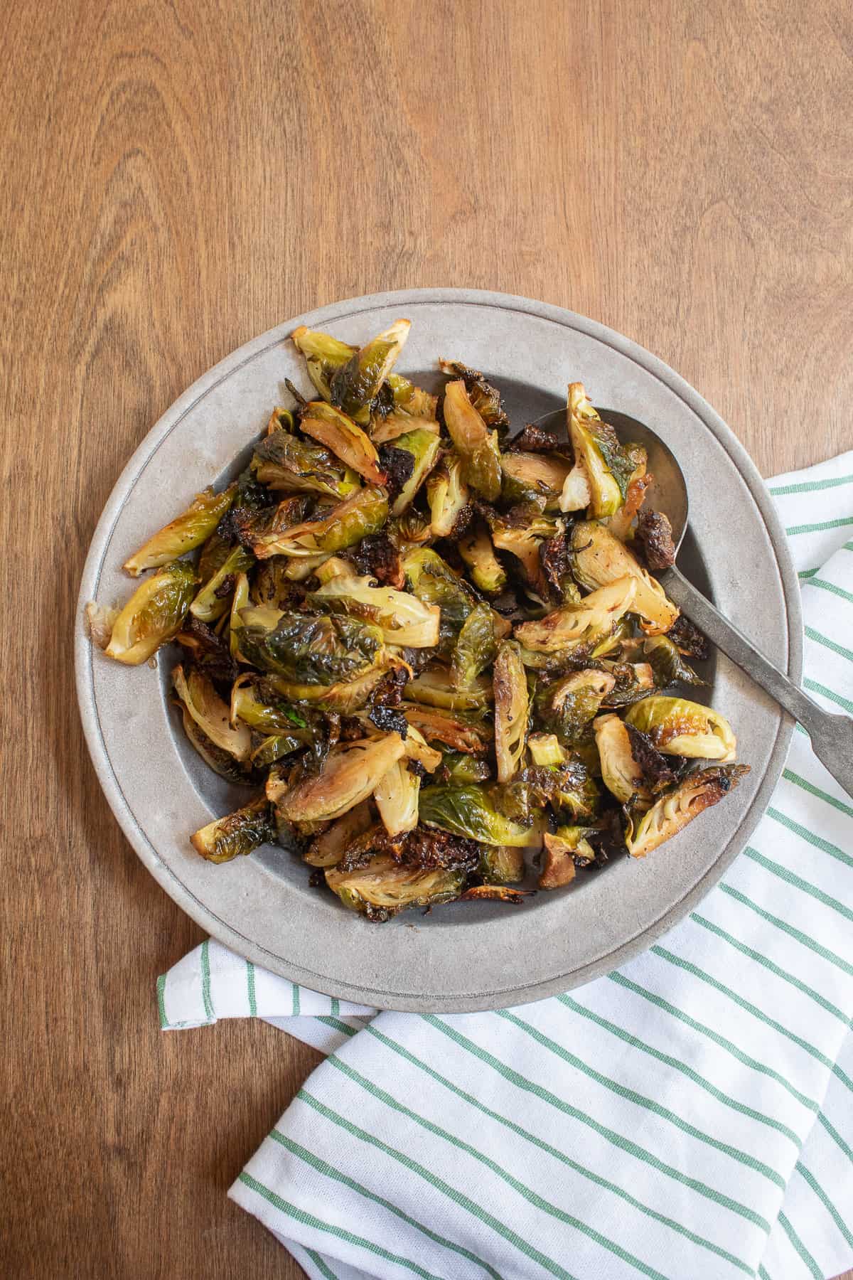 The finished brussel sprouts plated on a gray platter sitting on a wooden surface.