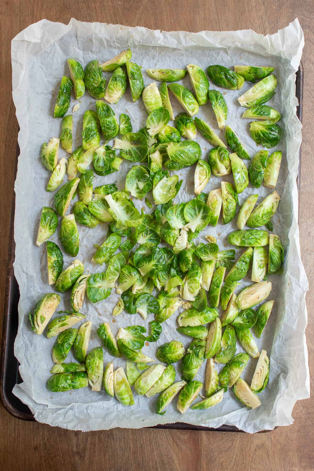 Brussel sprouts scattered over a parchment-lined sheet pan after tossing with the glaze.