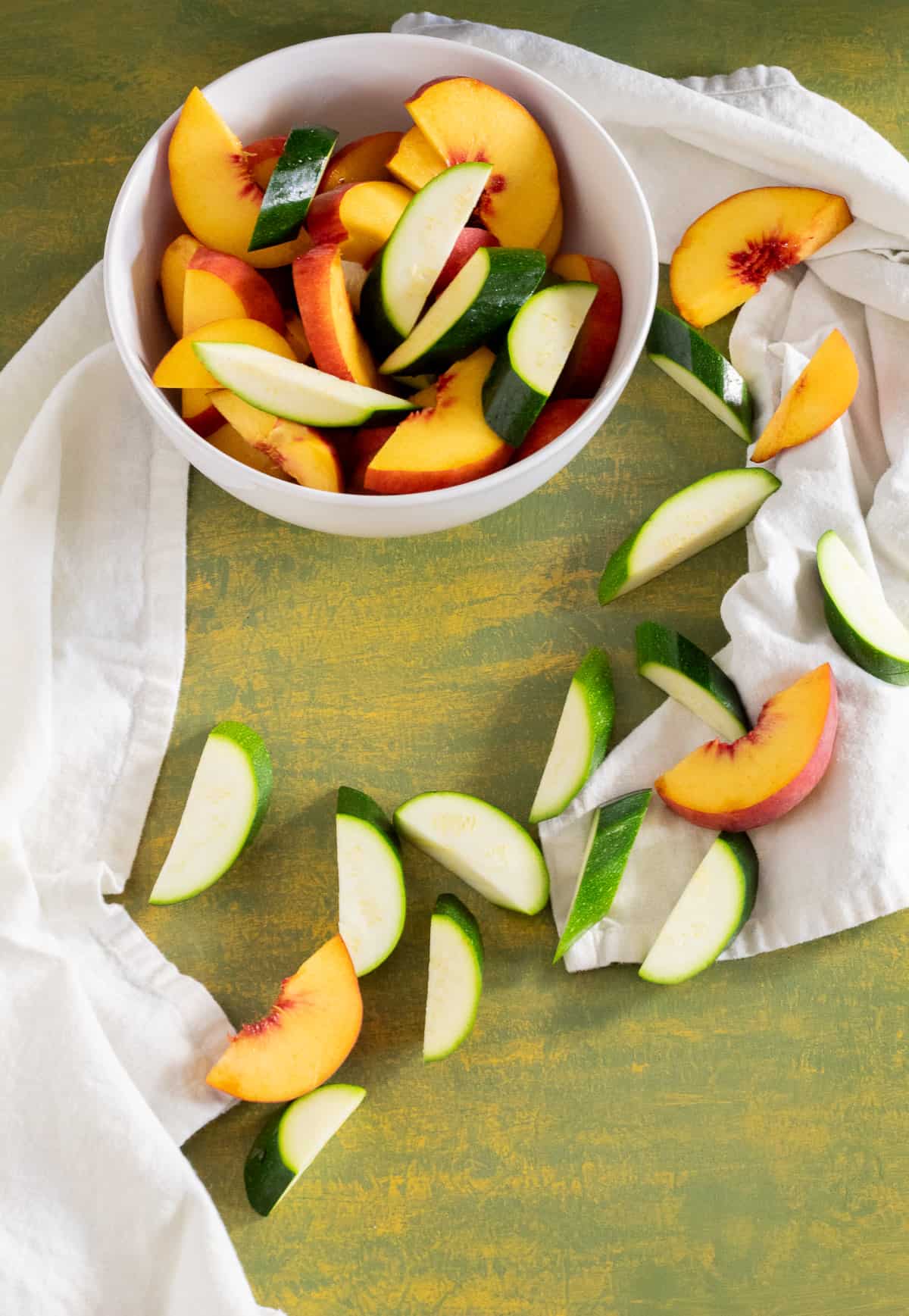 Peaches and zucchini are sliced in large enough pieces to nit fall through the grill grates and scattered over a green surface.