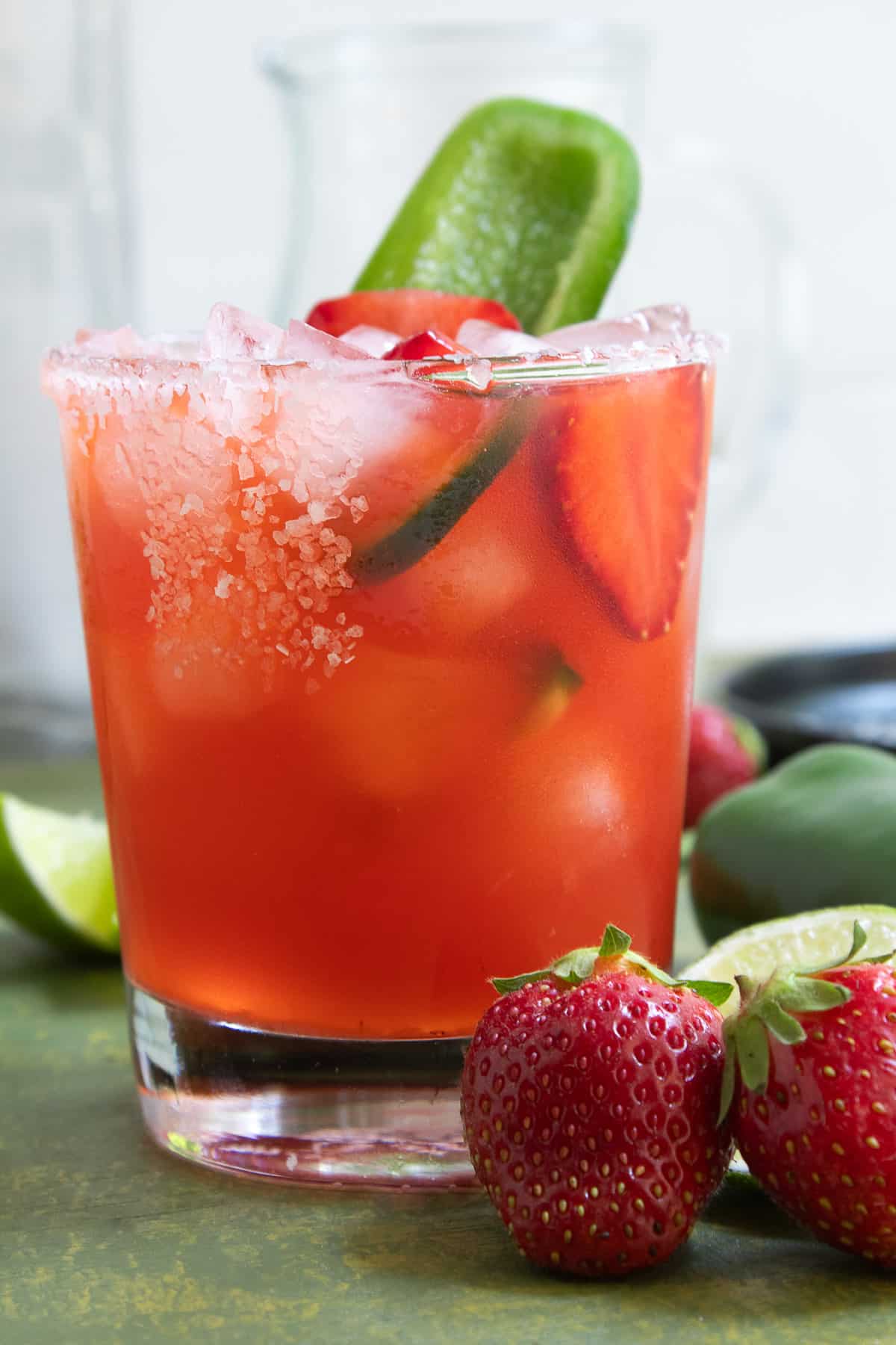 A close-up of a rocks glass with a salted rim and containing a red liquid and ice cubes