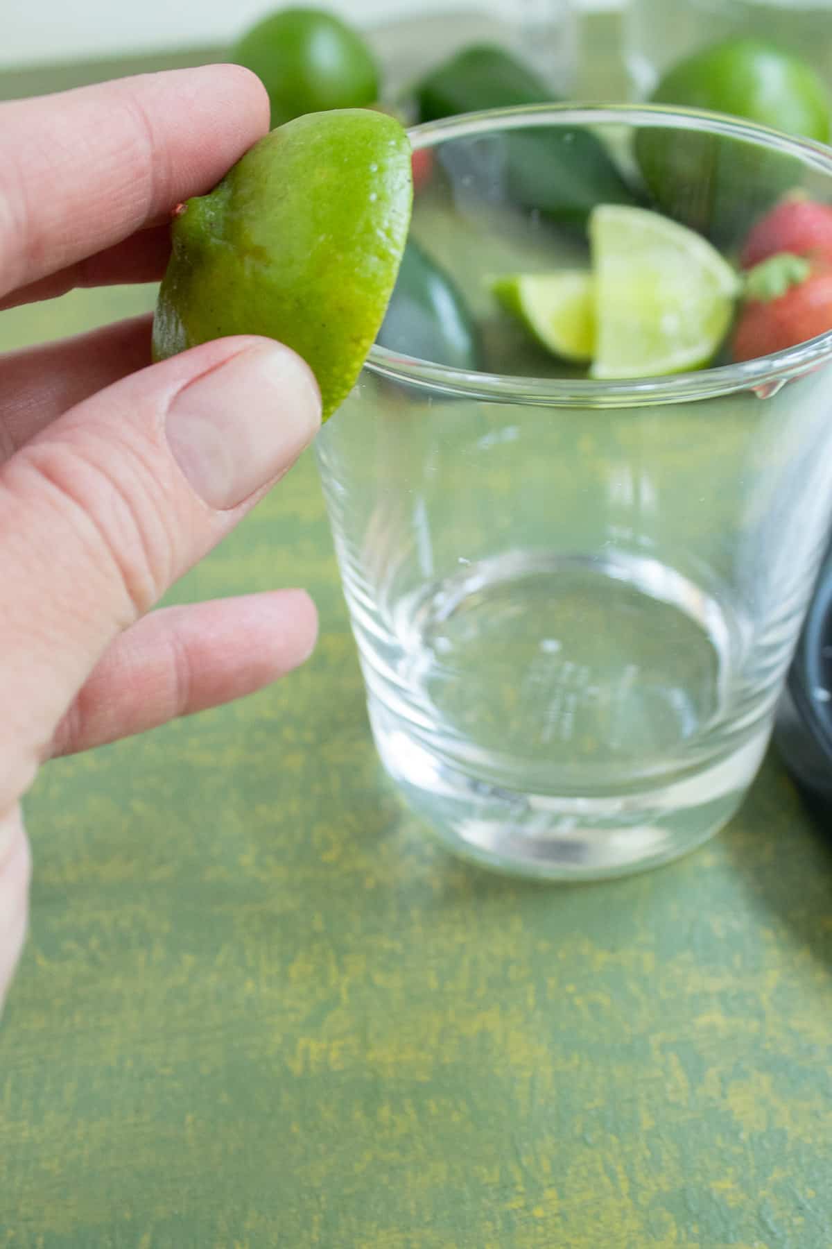 The rim of a rocks glass being rubbed with a half lime to moisten the edge.