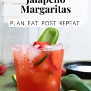 A rocks glass with a salted rim holds a red liquid and is garnished with a sliced strawberry and a slice of jalapeno. In a box at the top of the photo are the words, "Strawberry Jalapeno Margaritas" and "Plan. Eat. Post. Repeat."