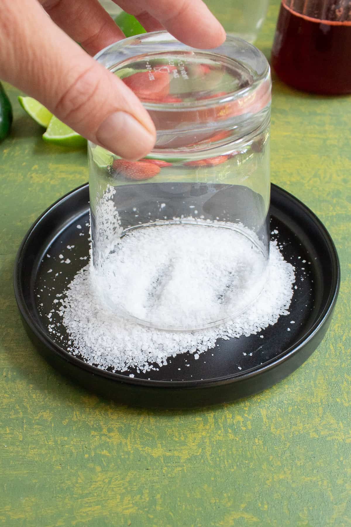 A rocks glass is upside down in a small dish of kosher salt on a green table.