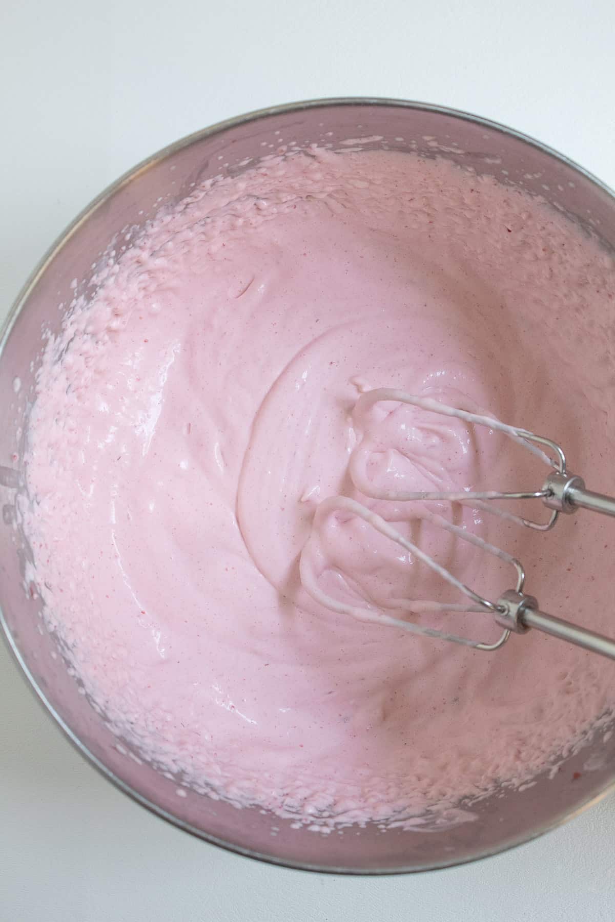 The whipped mousse and the beaters from the electric mixer sit in a stainless steel bowl.