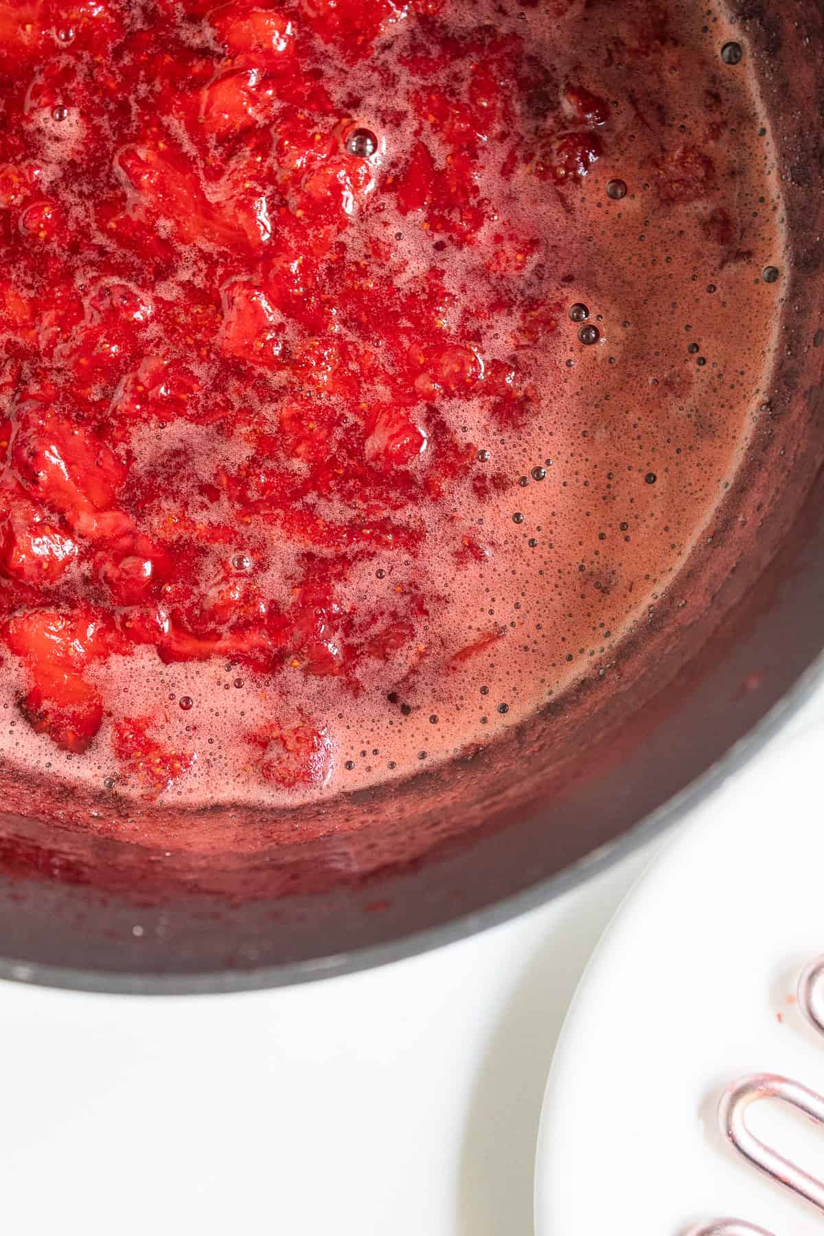 The cooked strawberry mixture is a vibrant red in a black saucepan.