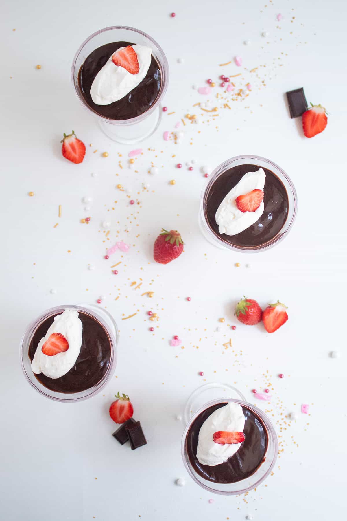 An overhead view of four servings of the finished mousse on a white background with sliced strawberries and chocolate pieces.