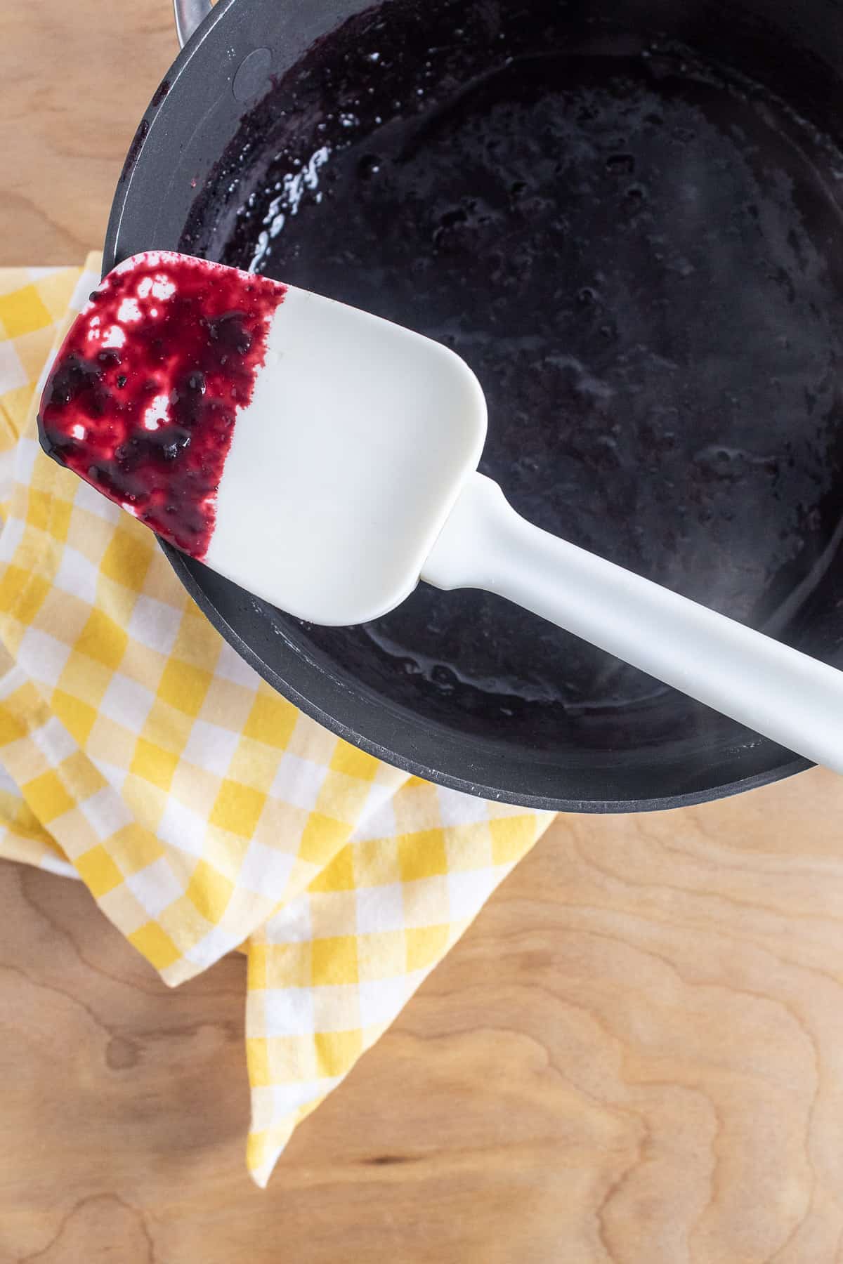 The dark red blueberry mixture coats a white silicone spatula.