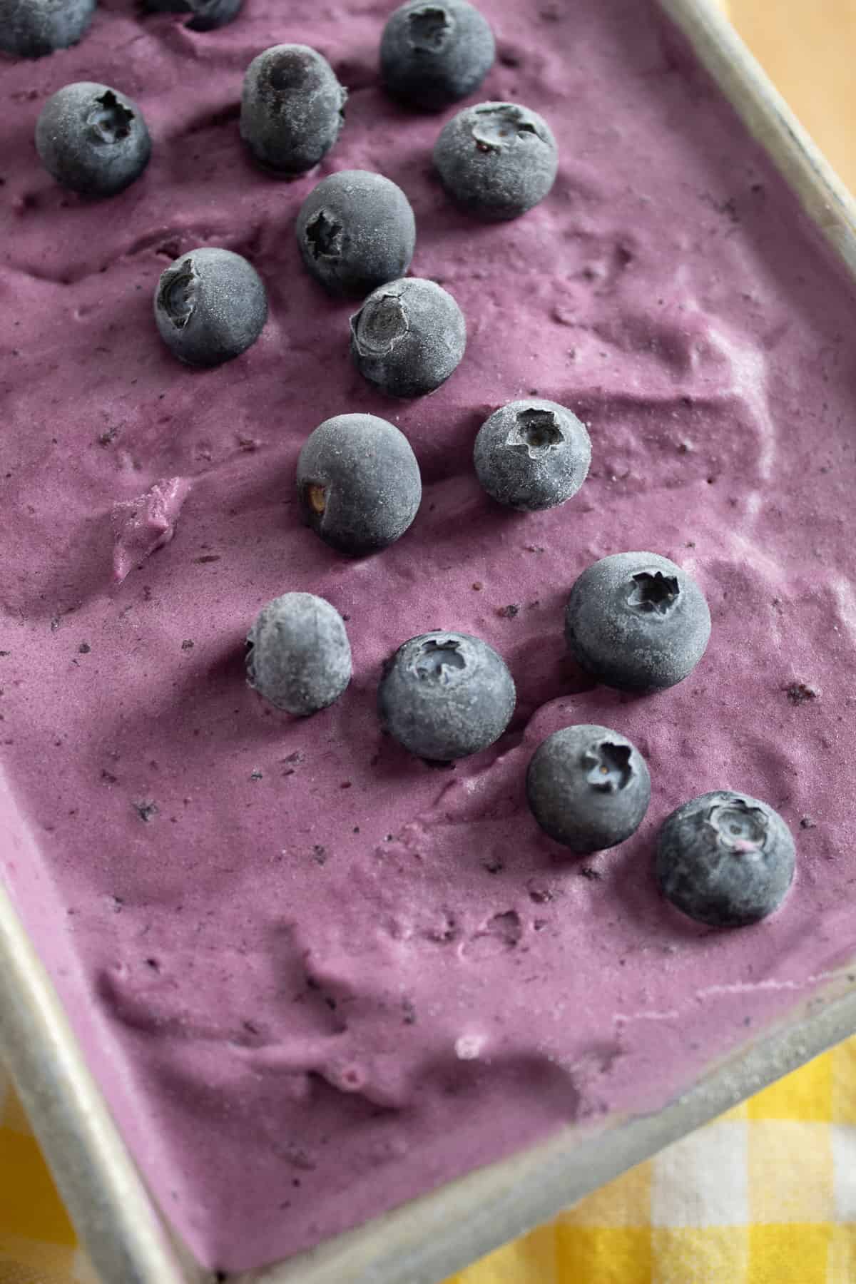 The frozen ice cream scattered with frozen blueberries in a loaf pan.