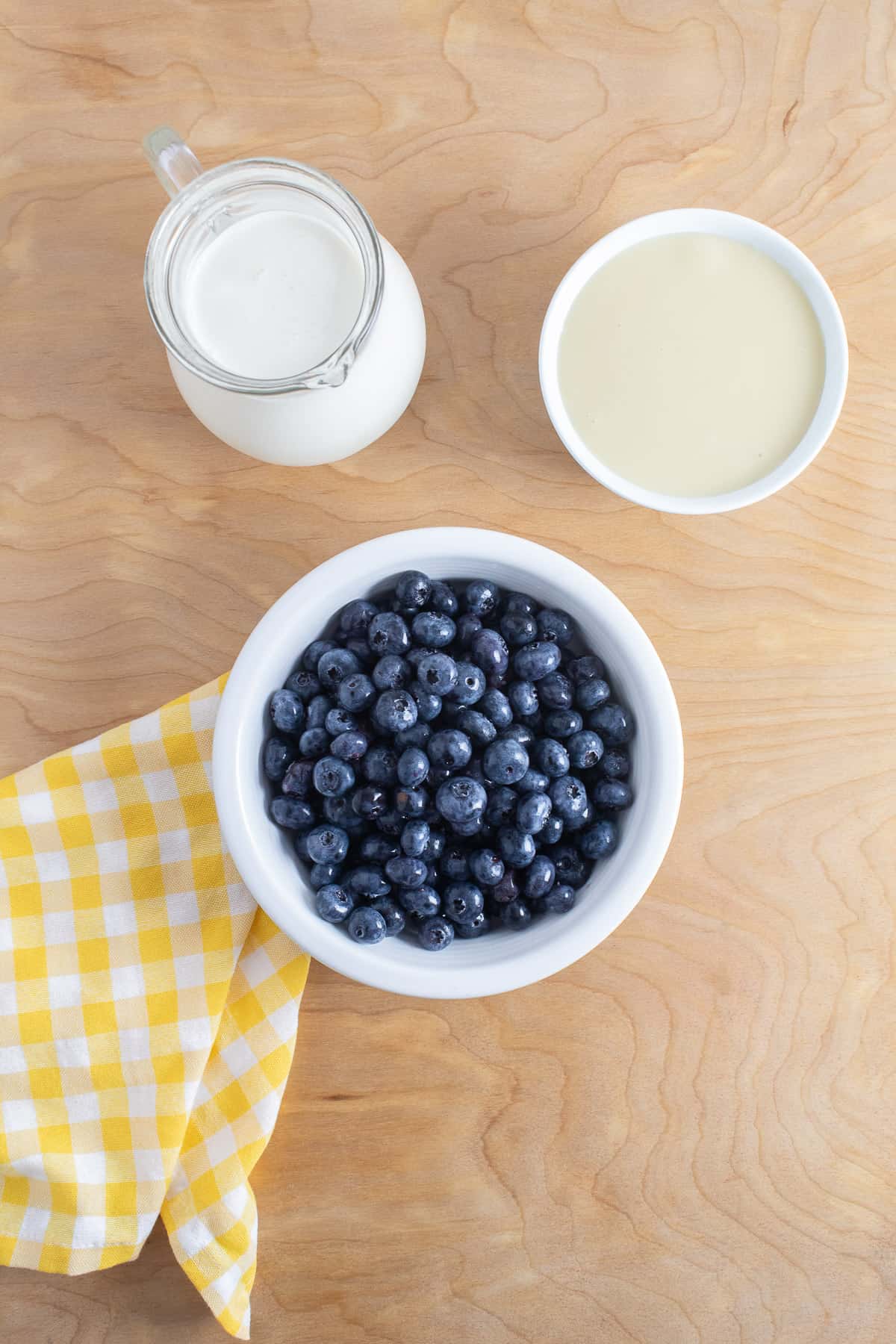 Ingredients for blueberry ice cream are displayed on a light wooden surface.