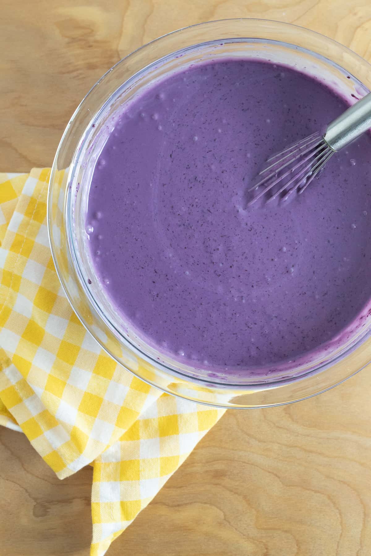 The cream, cooked blueberries, and sweetened condensed milk mixed together in a glass bowl, making a vivid purple mixture.