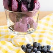 Scoops of vibrant magenta ice cream sit in a glass swerving bowl and are topped with a dark red syrup.