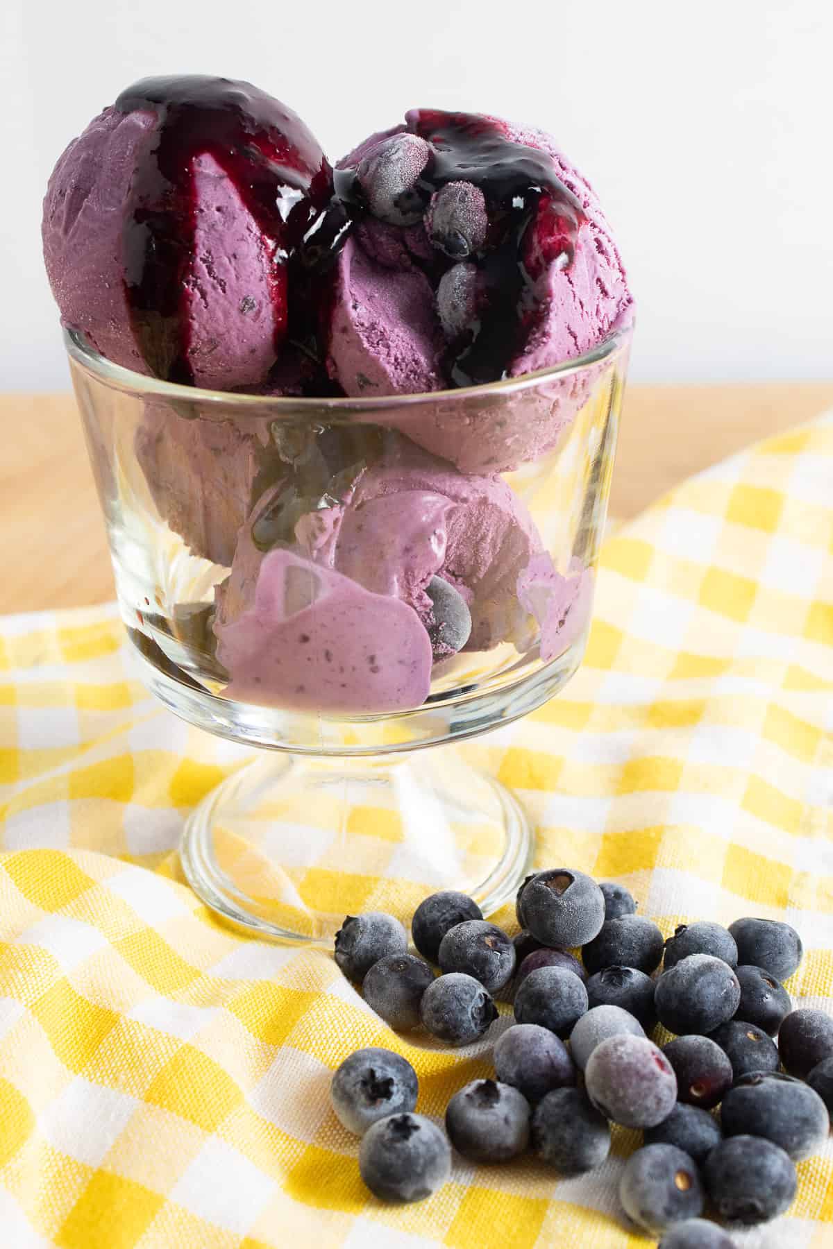 Scoops of vibrant magenta ice cream sit in a glass swerving bowl and are topped with a dark red syrup.