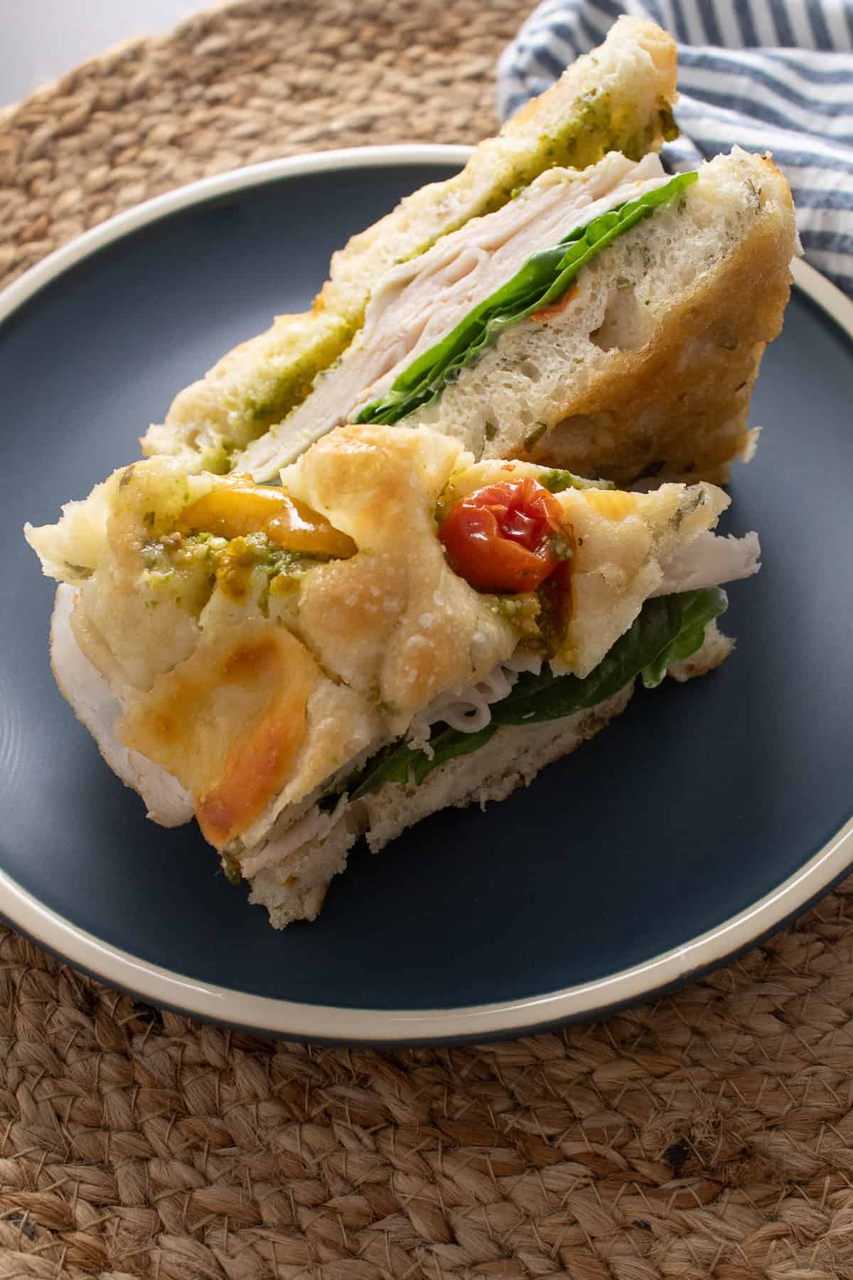 A turkey sandwich made on caprese focaccia bread sitting on a blue plate.