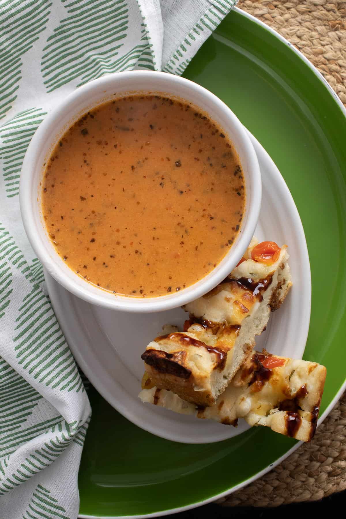 A bowl of tomato soup alongside two slices of caprese focaccia on a green tray.