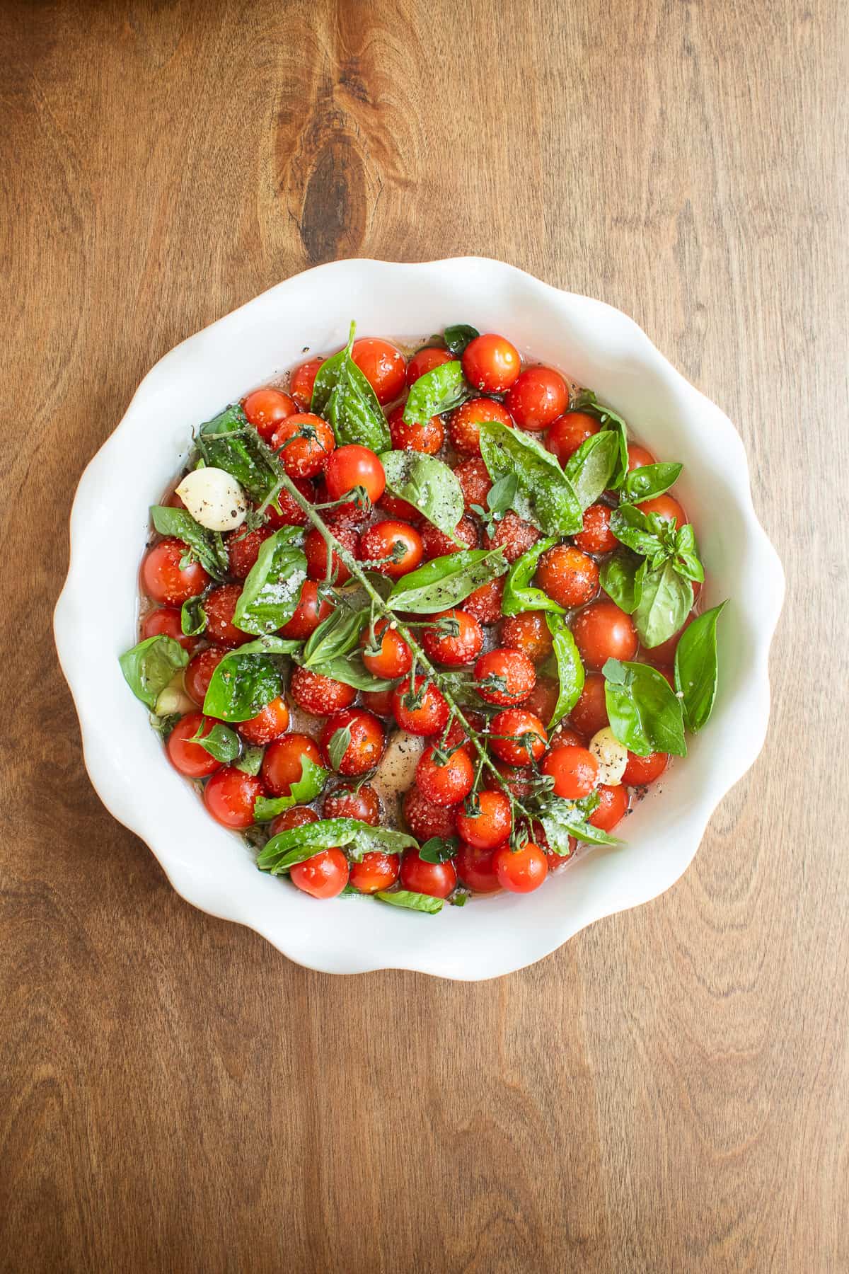 The tomatoes, basil, oregano, garlic, and oil arranged in a deep white pie dish.