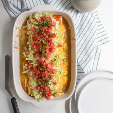 The finished casserole sits on a white table next to a white and green striped towel, a stack of plates, and a spatula.