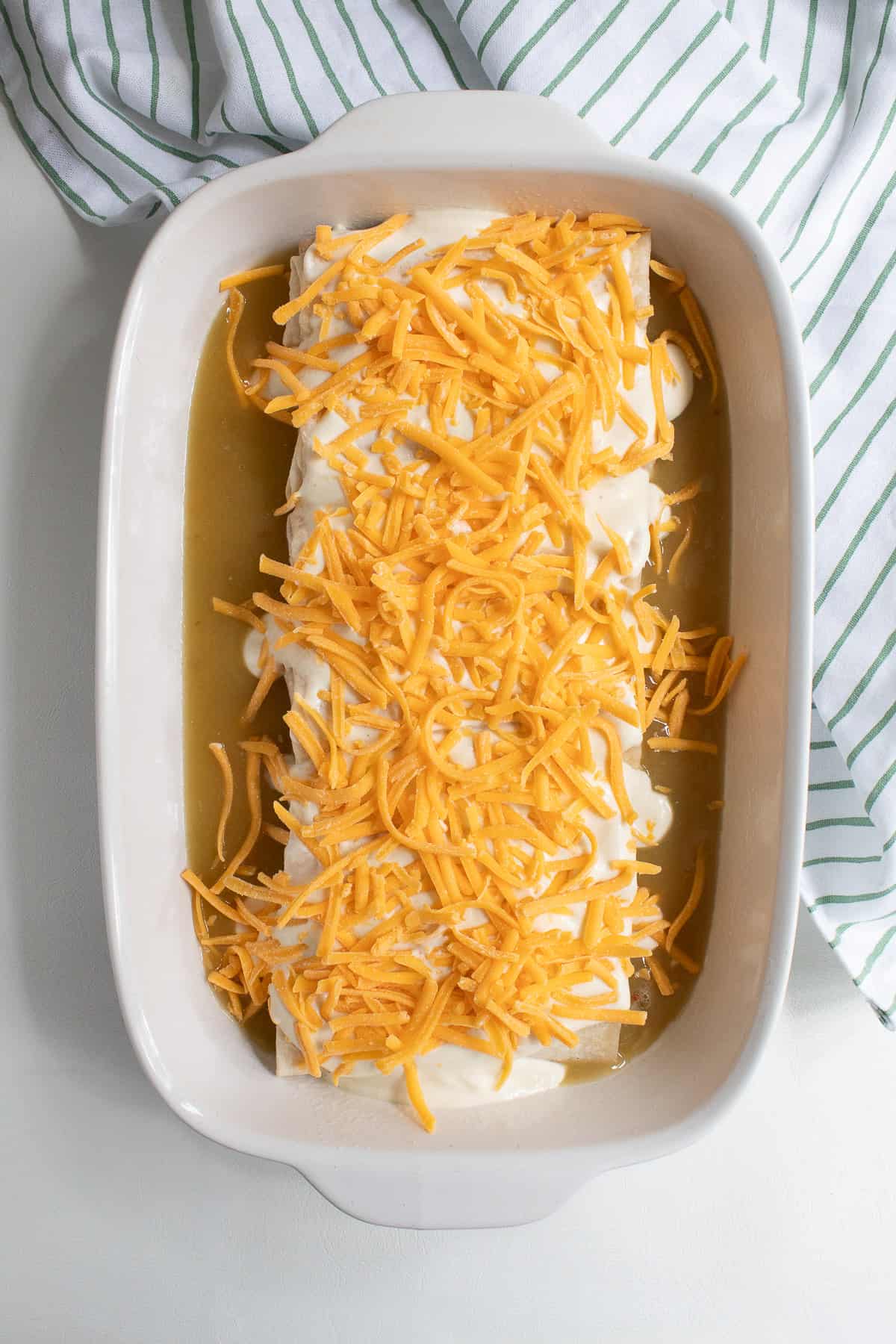 Cheese is sprinkled over the top of the sour cream layer on the burritos.